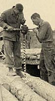 Two soldiers drilling a hole in a timber bridge.