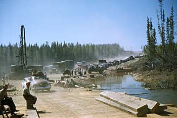 Traffic line of vehicles waiting to cross bridge at Rancheria River. 1948.
